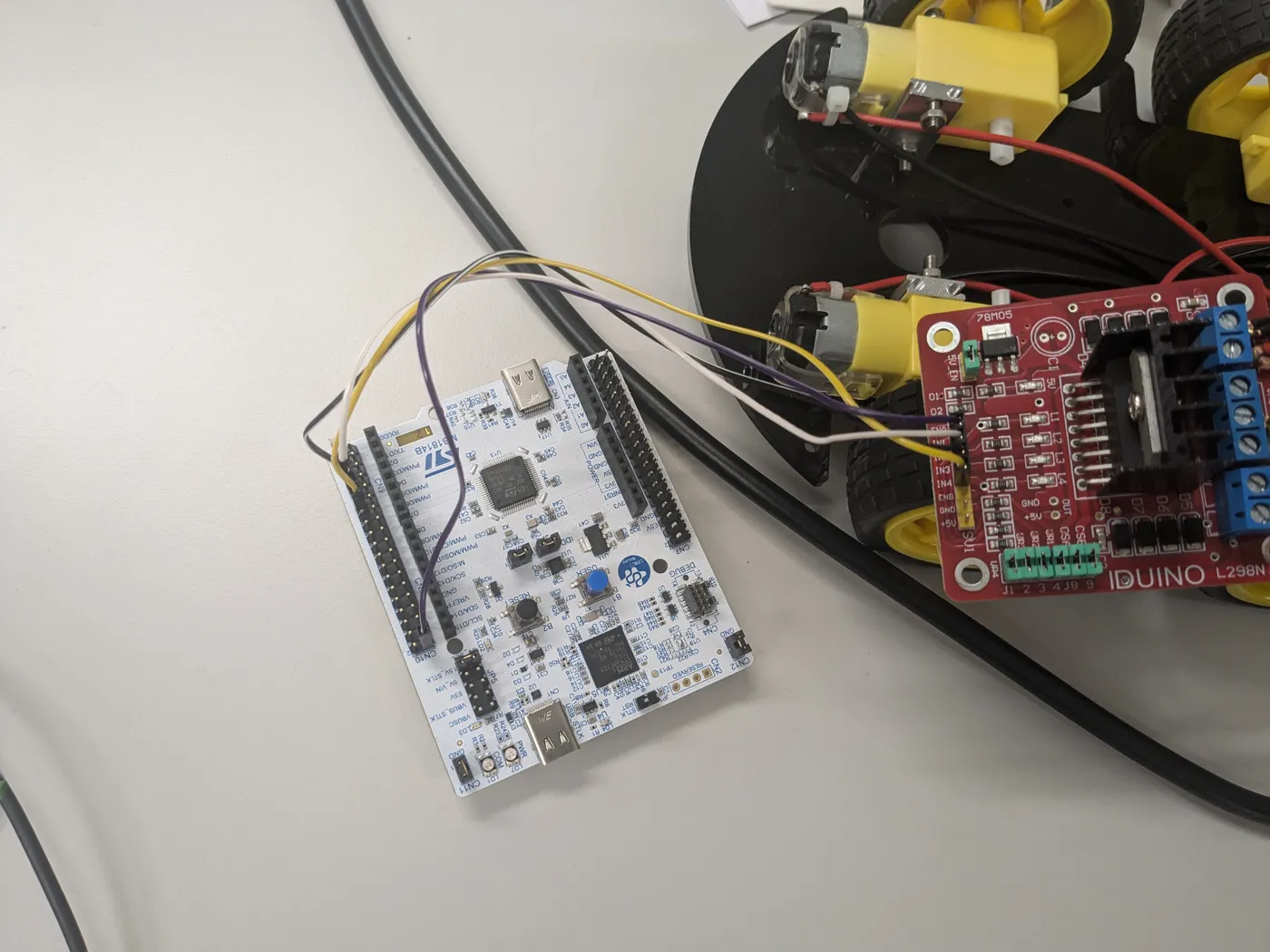 The underside of the robot chassis: an STM32 Nucleo board and a red motor driver board wired together with jumper leads above the wheels and motors.