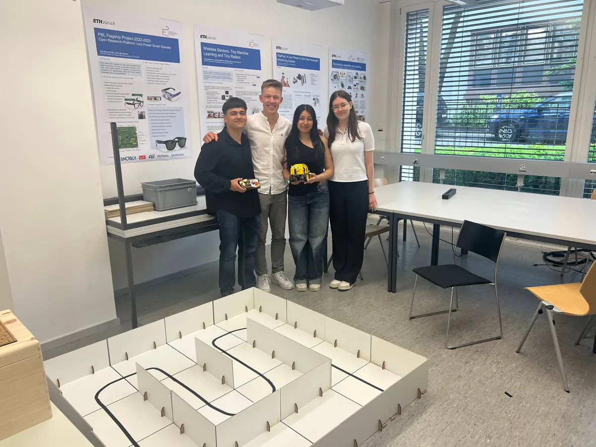 Four people standing behind the line-following track at the end of the project, one of them holding the robot.